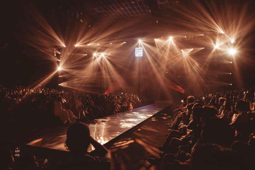 Desfile de moda em passarela iluminada diante de uma plateia.