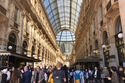 Pessoas circulam pelo interior da Galleria Vittorio Emanuele II, em Milão, sob a cobertura de vidro e a arquitetura histórica do local.