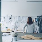Designer de moda trabalha em um estúdio cercada por moldes de costura e peças de roupa.