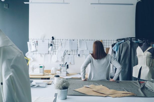 Designer de moda trabalha em um estúdio cercada por moldes de costura e peças de roupa.