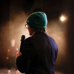 Pessoa segurando um microfone sob um refletor durante uma apresentação em um palco