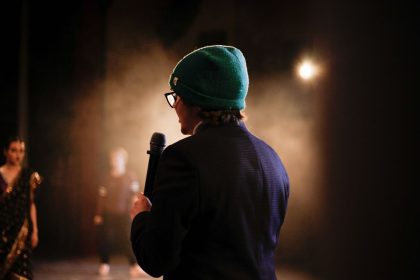 Pessoa segurando um microfone sob um refletor durante uma apresentação em um palco