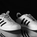 Tênis Adidas branco com listras pretas fotografado em close contra um fundo escuro