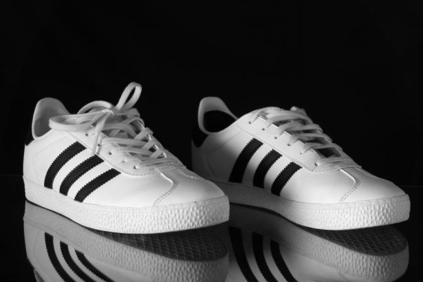 Tênis Adidas branco com listras pretas fotografado em close contra um fundo escuro