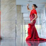 Mulher posa em um vestido vermelho de alta-costura em um corredor interno moderno.