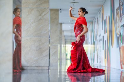 Mulher posa em um vestido vermelho de alta-costura em um corredor interno moderno.